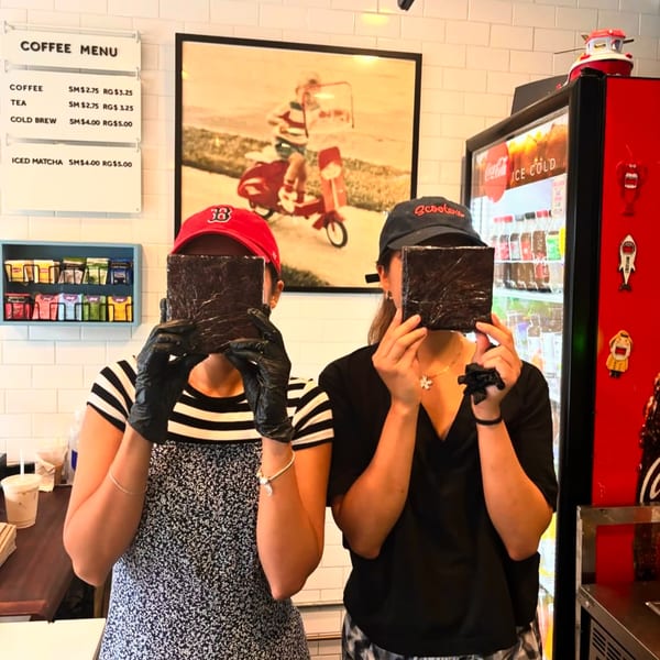 Two Scooters employees in hats and gloves hold up dark squares, obscuring their faces in the cafe.
