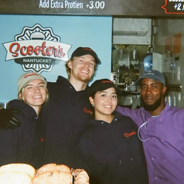 Four smiling Scooter's employees, three in black hoodies and one in a purple chef's coat, stand together.