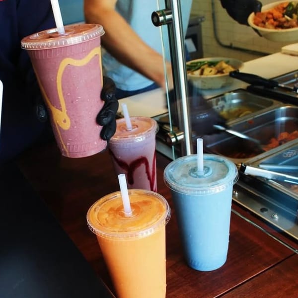 Four colorful smoothies and a person preparing food behind a counter at Scooters.