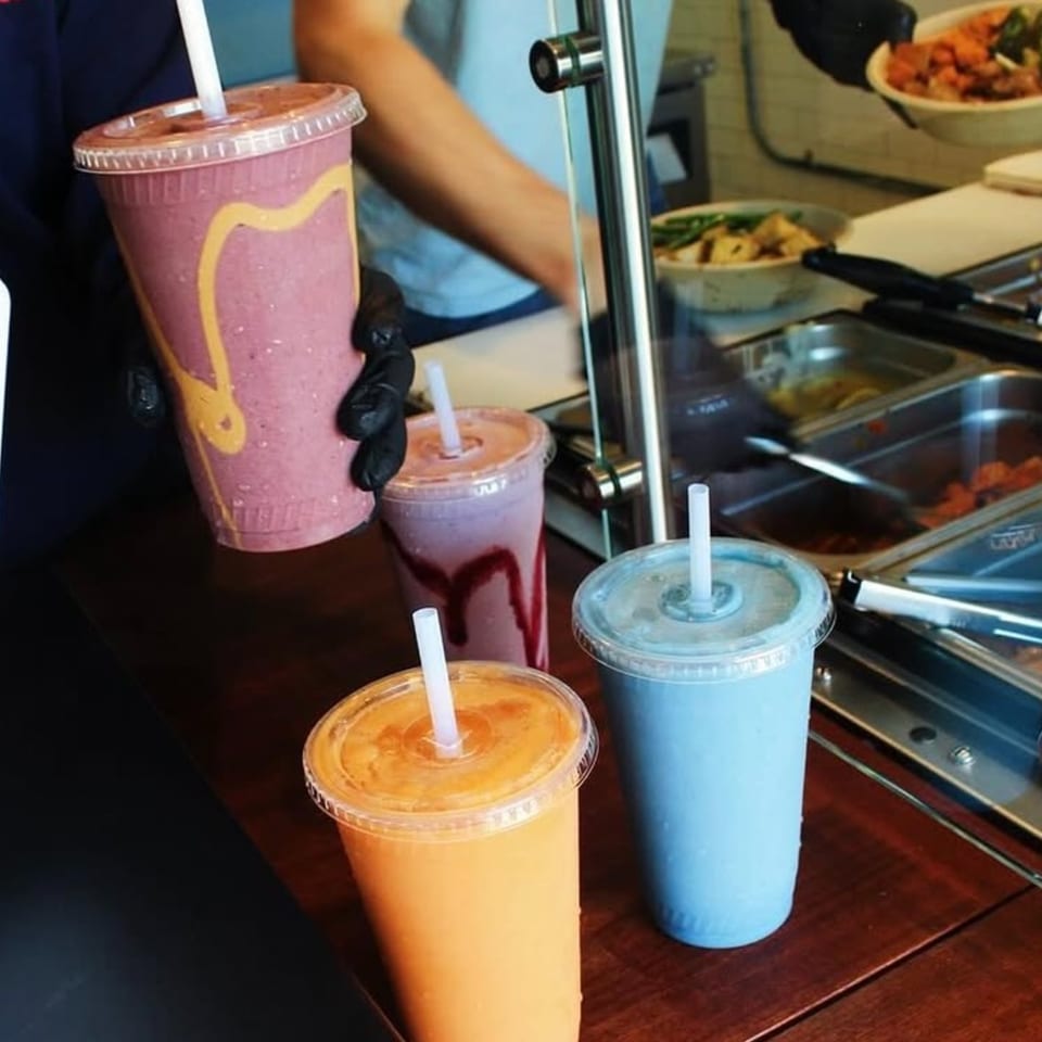 Four colorful smoothies and a person preparing food behind a counter at Scooters.