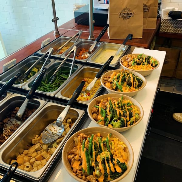 Scooters' healthy food bar with various ingredients and three prepared bowls topped with sauce.