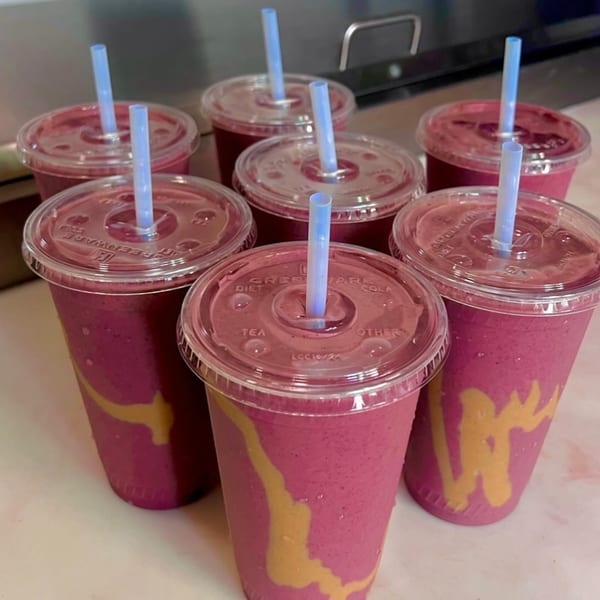 Six vibrant pink smoothies with peanut butter swirls and blue straws in clear plastic cups.