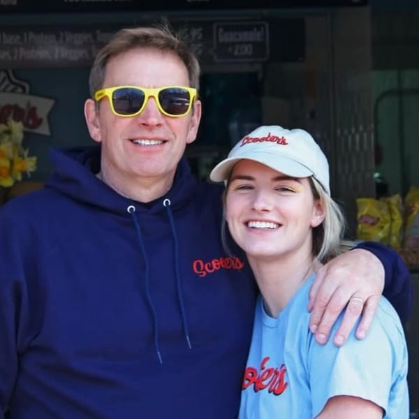 Smiling man in yellow sunglasses and woman in a Scooters hat and shirt, arm-in-arm.