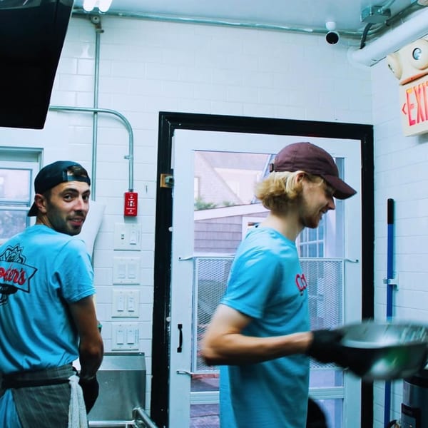 Two Scooters employees in blue shirts and hats working in a bright, tiled kitchen.