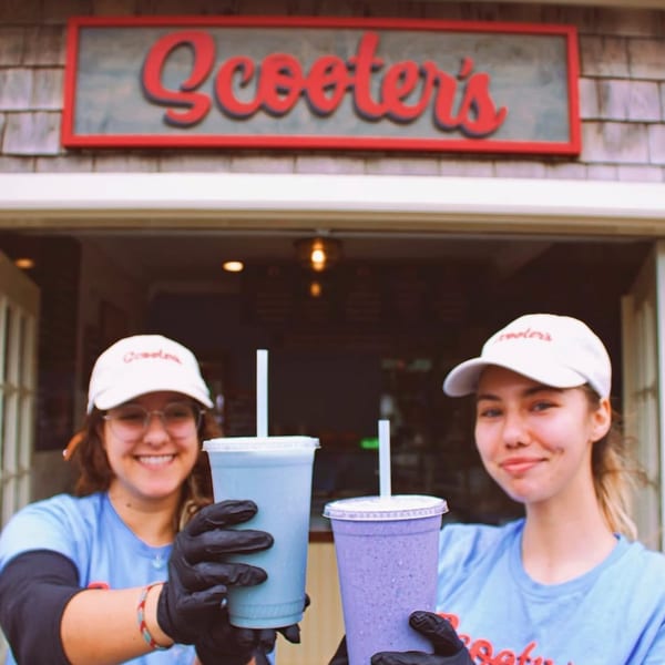 Two smiling Scooters employees in hats and gloves holding up blue and purple smoothies.