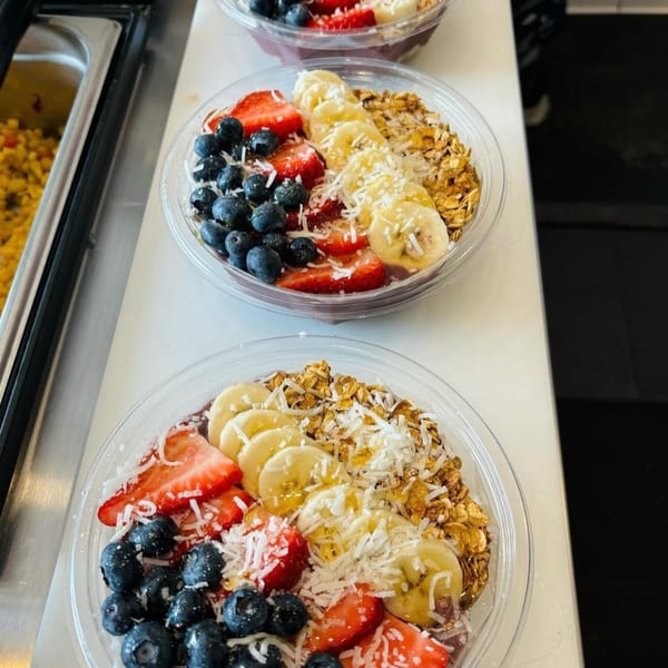 Three healthy acai bowls from Scooters, topped with blueberries, strawberries, bananas, granola, and coconut flakes.