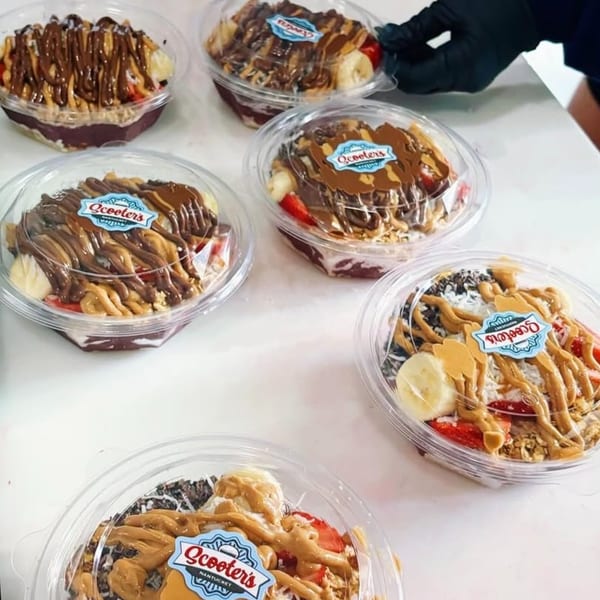 Multiple Scooters' healthy bowls with fruit, granola, and peanut butter on a white surface.